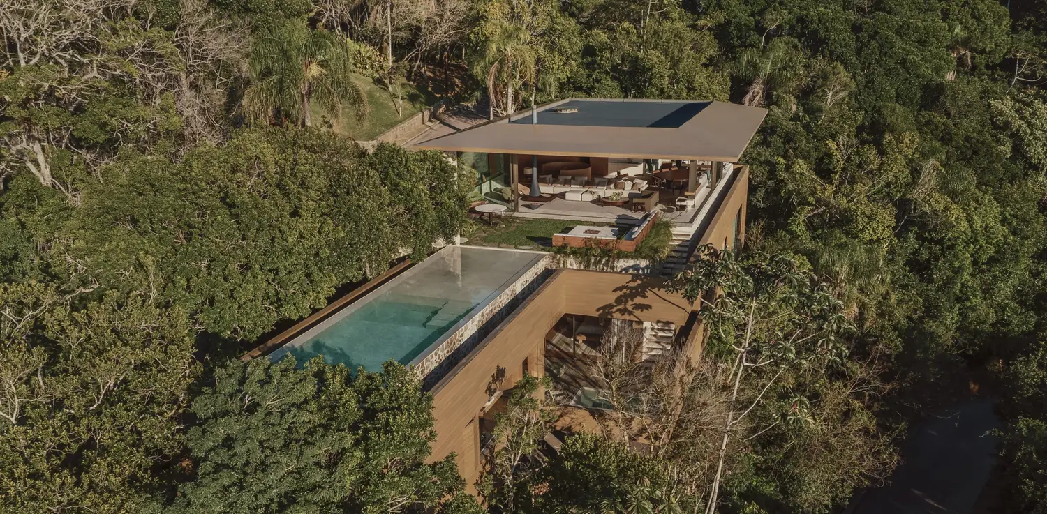 Casa contemporânea implantada na encosta da mata, com piscinas em dois níveis, vista do alto